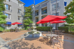 Exterior Outdoor Courtyard, 3 tiered fountain, bistro tables around fountain, 4 story buildings in background.