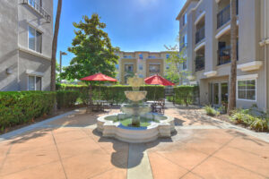 Exterior Outdoor Courtyard, 3 tiered fountain, bistro tables around fountain, 4 story buildings in background.