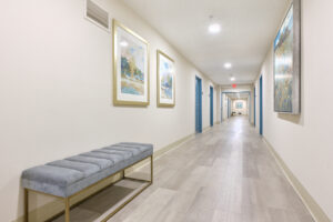 Interior Hallway, White walls, blue doors, velvet bench, abstract paintings with gold frames, wood floors.