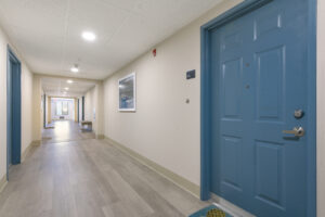 Hallway, off white walls, wood floors, blue doors, bench along wall.
